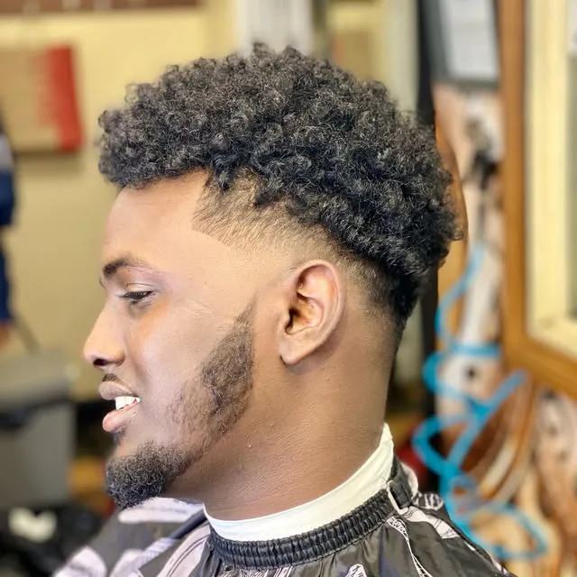 Curly top with a tapered fade and a shaped beard